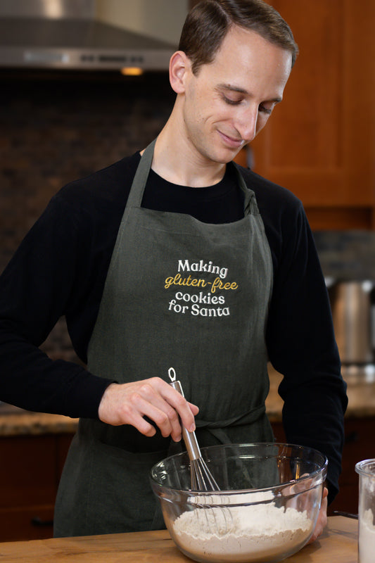 Man wearing green Christmas apron with "Making gluten-free cookies for Santa"