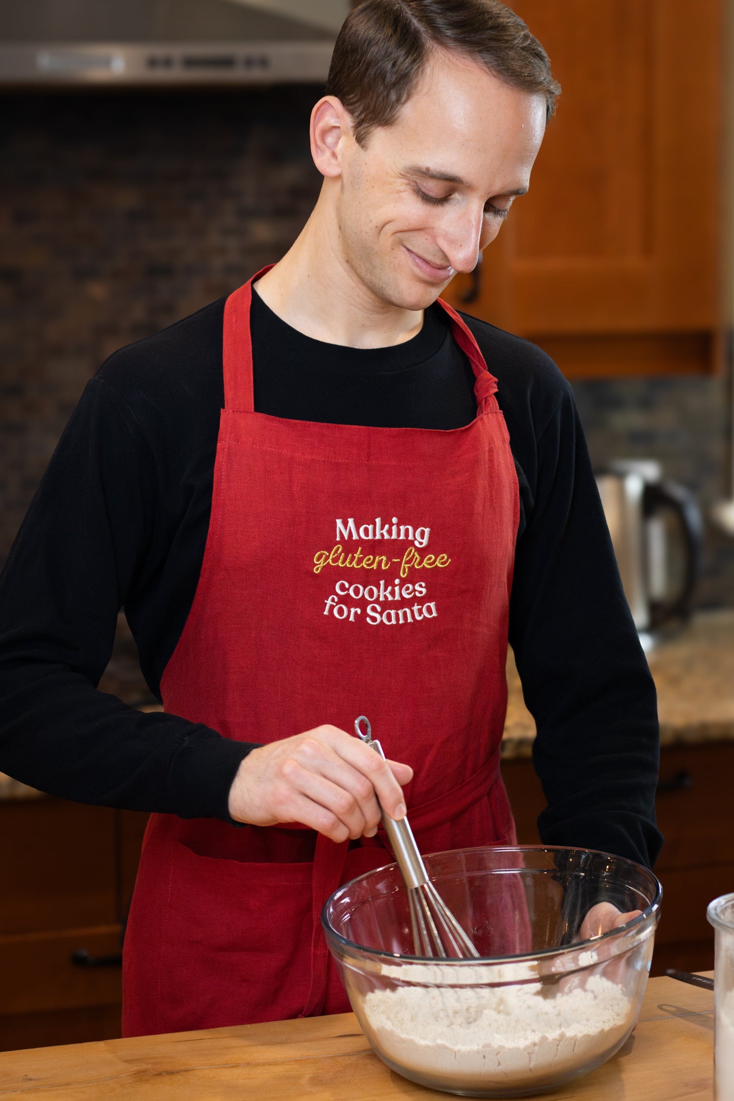 Man wearing red Christmas apron with "Making gluten-free cookies for Santa"